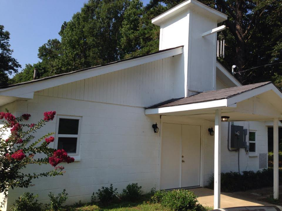 A white church building with a blooming crepe myrtle nearby