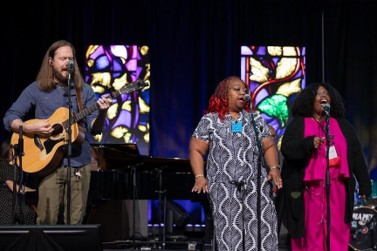 Group of musicians on stage in front of stained glass windows