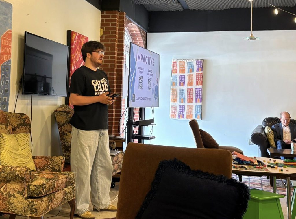 Person wearing a Get Loud Arkansas t-shirt and khakis standing at the front of a room speaking to an audience